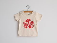 This super-soft unisex kids tee was designed with love and screen printed by hand in-house. Original woodland mushroom illustration is printed in crisp red ink on 100% organic cream cotton fabric. Made in the USA and hand-printed in our Ohio studio. Perfect for outdoorsy little ones, adventurous tots, nature lovers, and fairy gardeners! All artwork is original. Sizes available in: * 3-6 Months * 6-12 Months * 12-18 Months * 18-24 Months * 2T * 4T * 6T * Youth Small * Youth Medium * Youth Large N Playful Organic Cotton Graphic T-shirt, Playful Organic Cotton T-shirt With Graphic Print, Playful Organic Cotton Graphic Print T-shirt, Cute Organic Cotton T-shirt With Screen Print, Cotton Graphic Tee With Mushroom Design, Cute Short Sleeve Top With Mushroom Print, Summer Cotton T-shirt With Mushroom Design, Cotton Summer T-shirt With Mushroom Design, Cotton Graphic Tee With Mushroom Print