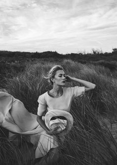 a woman sitting in tall grass on top of a field