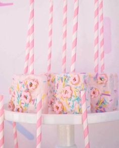 pink and white birthday cake with sprinkles on it, surrounded by candles