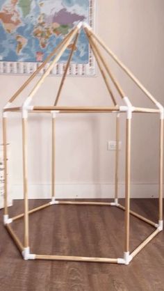 a house made out of wooden sticks on top of a hard wood floor in front of a map