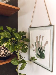 a potted plant sitting on top of a wooden shelf next to a framed handprint