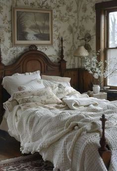 a bed sitting in a bedroom next to a window covered in white blankets and pillows