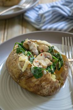 a white plate topped with a baked potato covered in cheese and spinach next to a fork