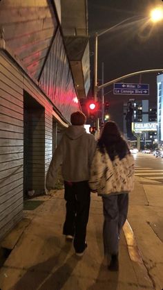 a man and woman walking down the sidewalk in front of a building at night time