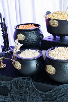 three black caulders filled with popcorn sitting on top of a purple table cloth