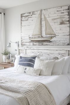 a white bed topped with pillows and blankets next to a painting on the wall above it