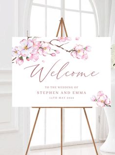 a welcome sign with pink flowers on it in front of a white wall and window