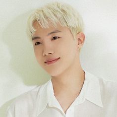 a man with blonde hair wearing a white shirt posing for a photo in front of a white wall