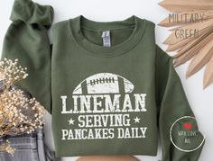 a green shirt with the words lineman serving pancakes daily on it next to some flowers