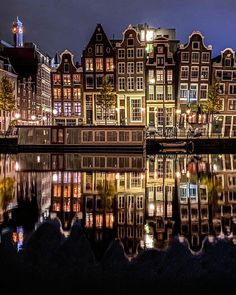 many buildings are lit up at night by the water's edge with lights reflecting in the water