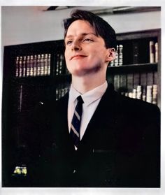 a man wearing a suit and tie standing in front of bookshelves with his eyes closed