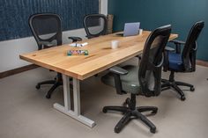 an office table with four chairs and a laptop on it in front of a blue wall