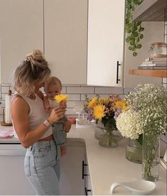 a woman holding a baby in her arms while standing next to a counter with flowers