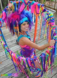 a woman with colorful hair and costume sitting on a wooden deck holding onto streamers