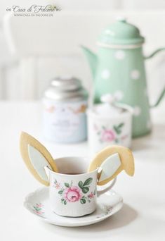 a teacup with some cookies in it on a table next to a tea pot