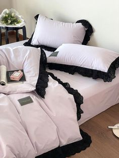 a bed with white sheets and black ruffles on the pillow cases, along with two pillows