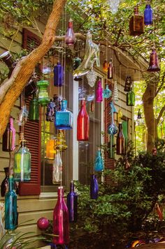 colorful glass bottles are hanging from the side of a house in front of a tree