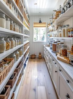 a kitchen filled with lots of white shelves and wooden flooring next to a window