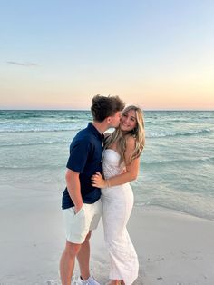 a man and woman hugging on the beach at sunset with ocean in the back ground