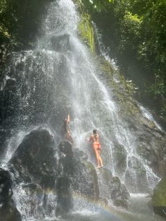 two people are swimming in the water near a waterfall