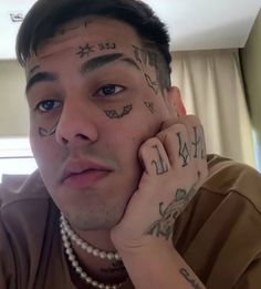 a young man with tattoos on his face and hand next to his ear is looking at the camera