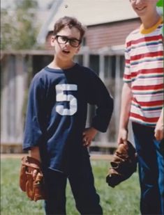 two young boys standing in the grass with baseball mitts and gloves on their hands