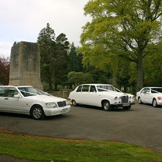 three white cars parked in a parking lot next to a monument and trees on a cloudy day