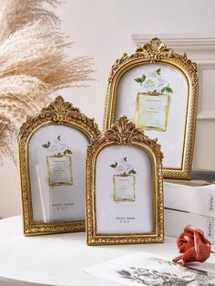 three ornate gold frames sitting on top of a white table next to a vase with flowers