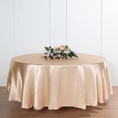 a round table with a flower centerpiece on it's top, in front of a white wall