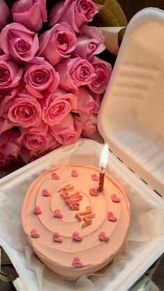 a pink birthday cake sitting on top of a white box next to flowers and a candle