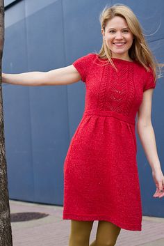 a woman standing next to a tree in front of a building wearing tight brown pants and a red dress