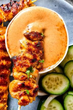 chicken skewers with dipping sauce and cucumber slices on a blue plate