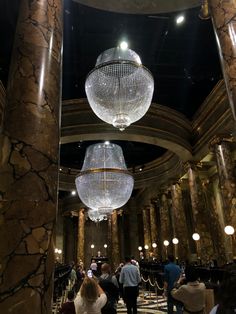 people are walking around in the lobby of a building with chandeliers hanging from the ceiling