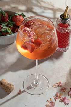 a close up of a drink in a wine glass on a table with strawberries