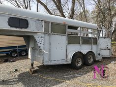 an old white horse trailer is parked in the gravel near some trees and other items