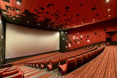 an empty auditorium with red seats and a projector screen