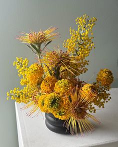 a vase filled with yellow flowers sitting on top of a white table next to a wall