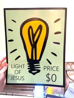 a person holding up a sign with a light bulb on it that says light of jesus $ 50