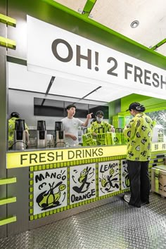 two men standing in front of a green and white food stand with fresh drinks on the counter