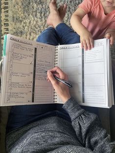 a woman sitting on the floor reading a book while holding a cell phone