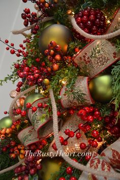 a christmas tree decorated with red and gold ornaments, berries, pine cones and burlocks