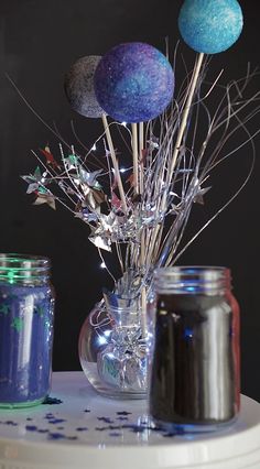 a vase filled with blue and purple balls sitting on top of a table next to two jars