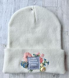 a white beanie with flowers on the front and an embroidered label that says removed from knitting