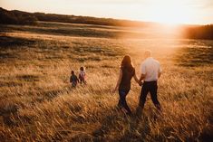 a man and woman holding hands while walking through a field with two children on the other side