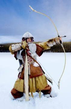 a woman dressed in medieval clothing holding a bow and arrow while standing in the snow