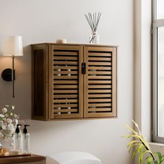 a wooden cabinet hanging on the wall next to a vase with flowers and reeds