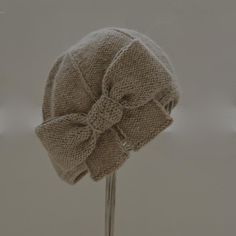 a knitted hat with a bow sitting on top of a metal pole in front of a gray background