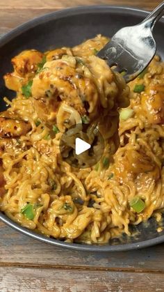 a bowl filled with noodles and meat on top of a wooden table next to a fork