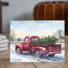 a red truck with a christmas tree in the back is sitting on a table next to some books