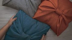 four different colored pillows on the floor with one person's hand reaching for them